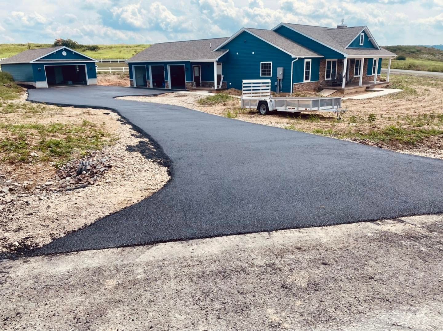 Blue house and detached garage with a curved asphalt driveway in a sandy coastal landscape.
