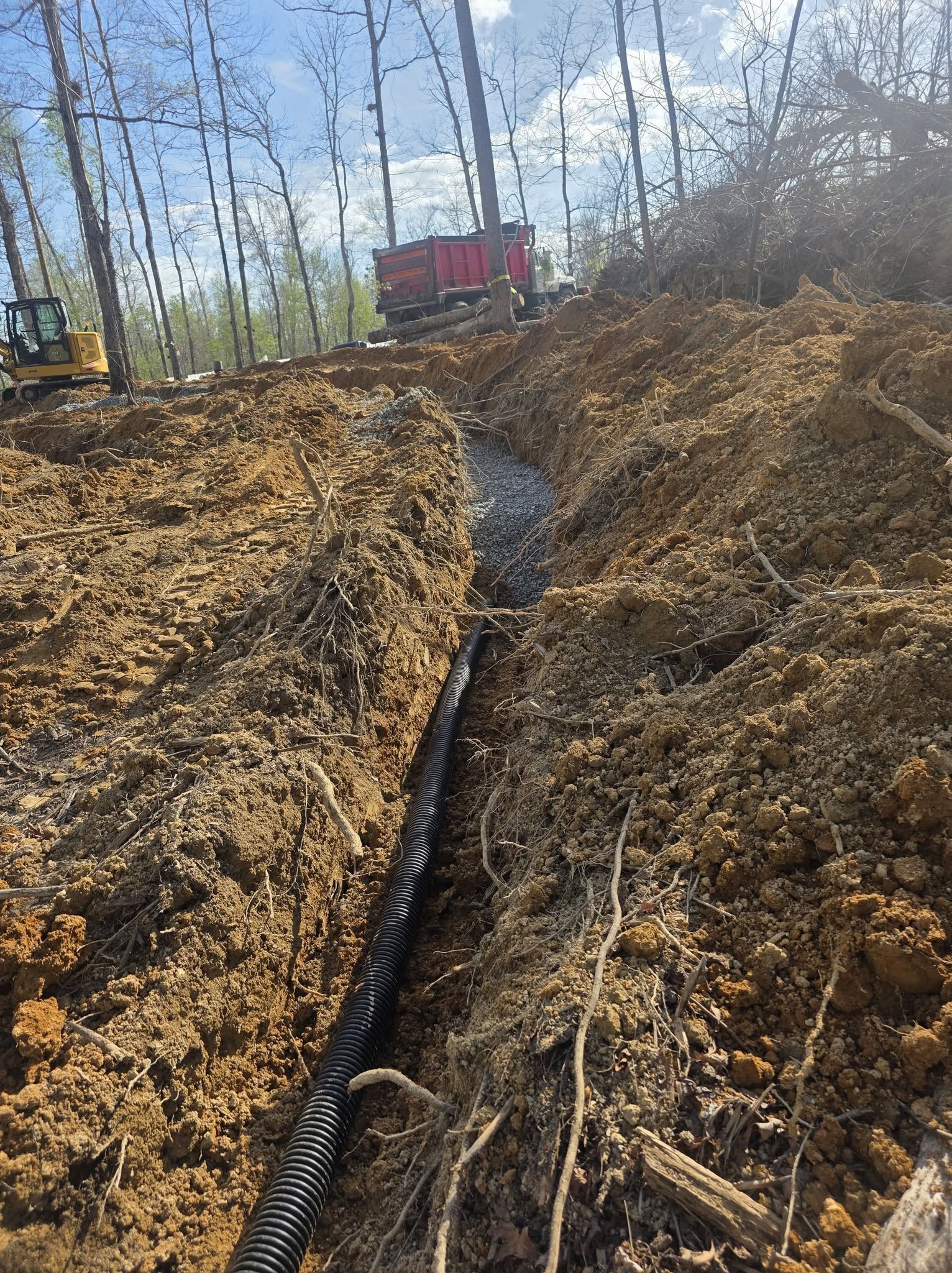 Excavator working in a narrow muddy trench in a wooded construction site