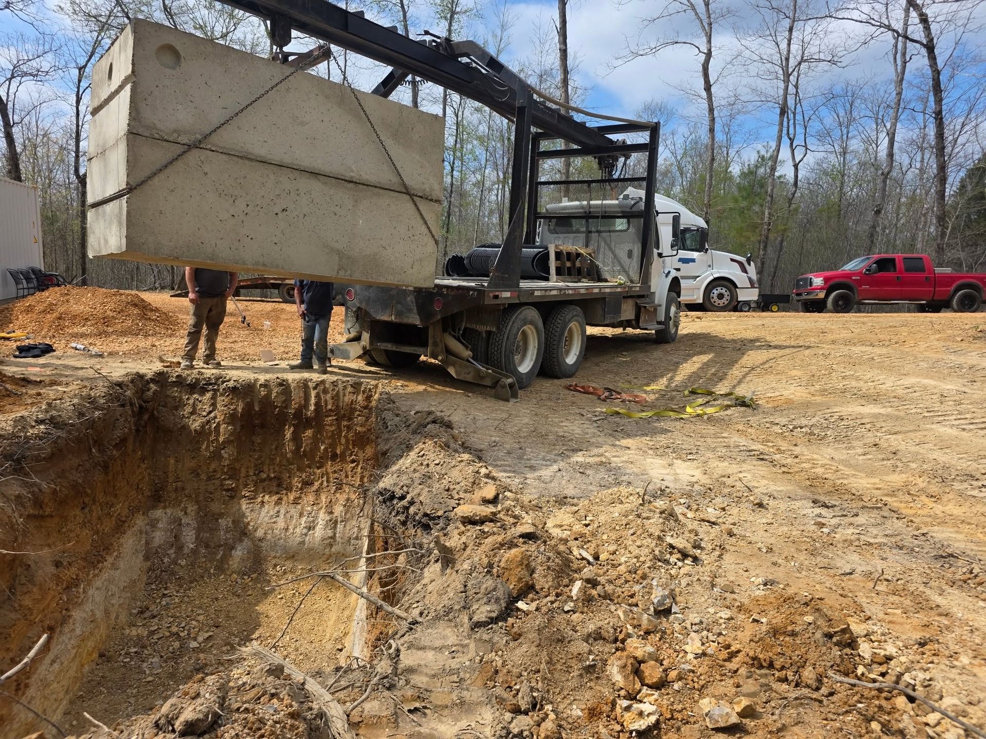 Truck lifting a concrete tank over a large excavation at a dirt construction site