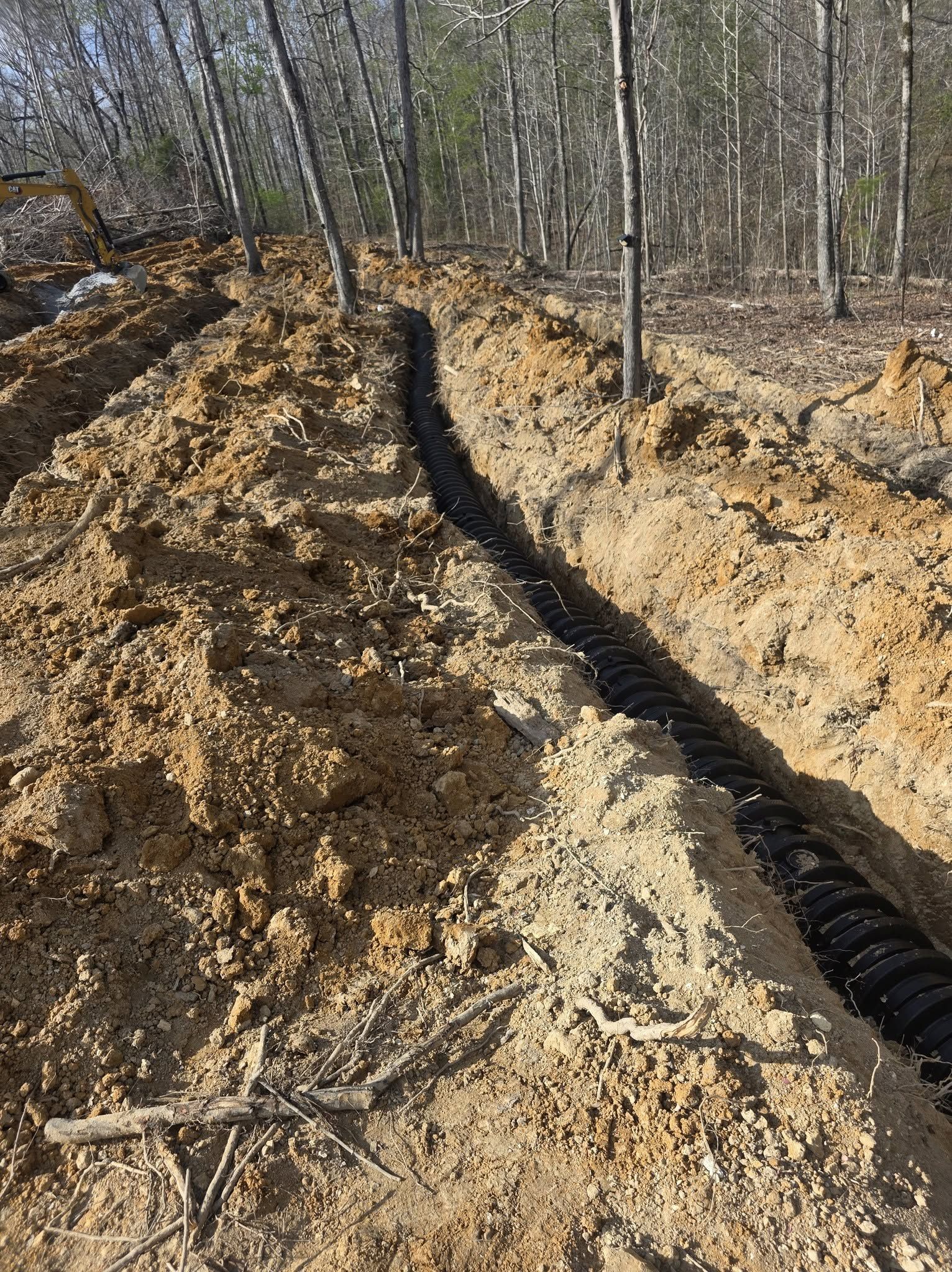 Dirt construction trench with black drainage pipe running along the ground in a wooded area