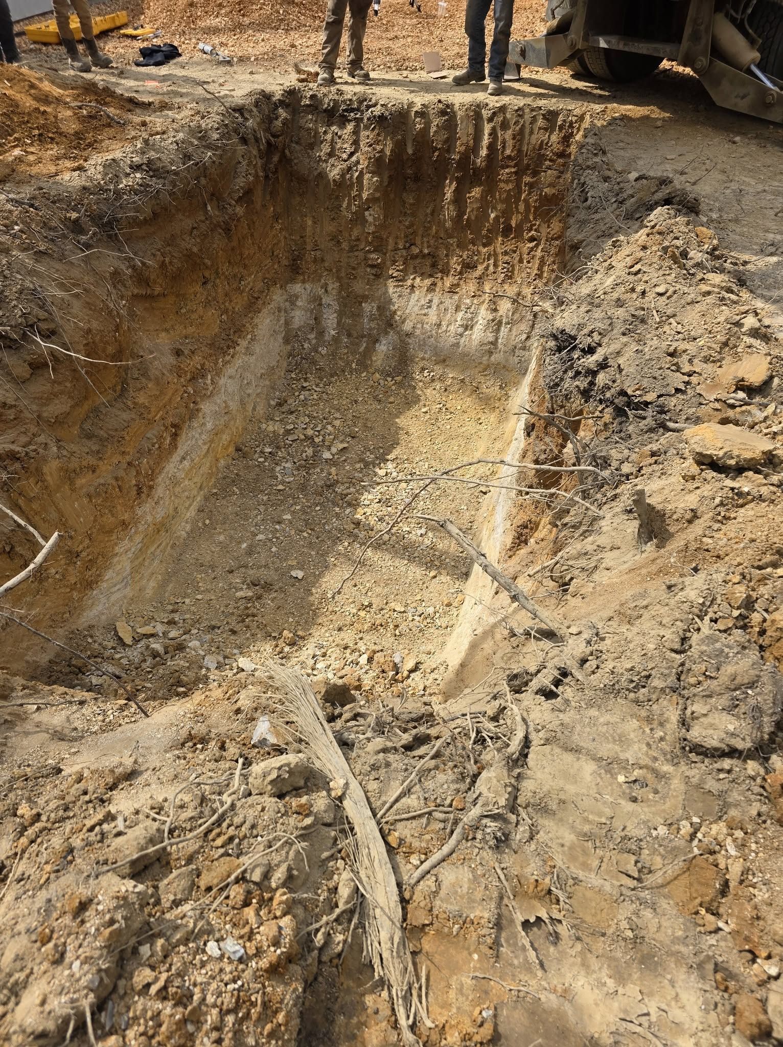 Large muddy excavation pit with standing water and a sloped dirt trench at a construction site
