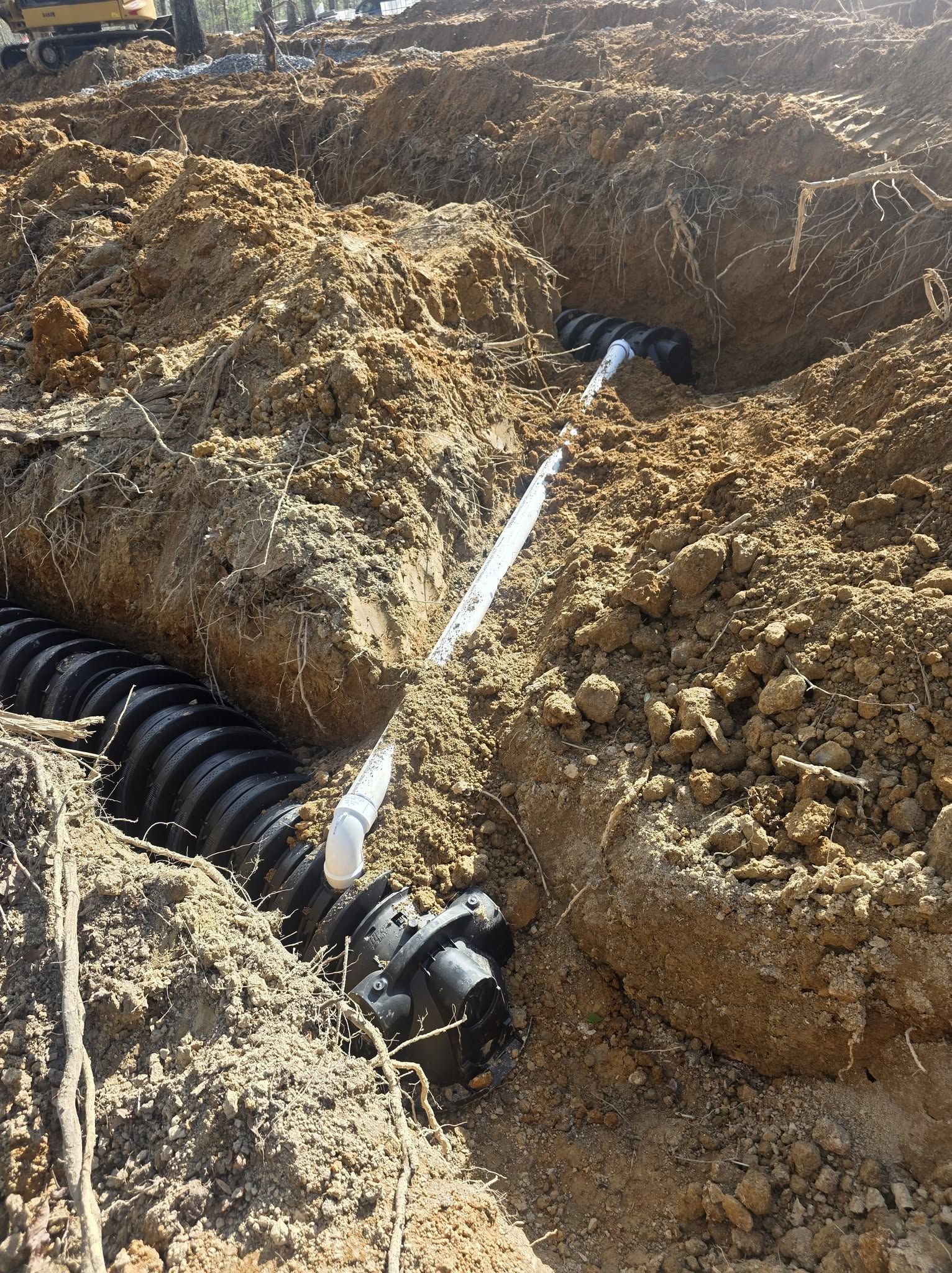 Black corrugated pipe laid in a dirt trench with muddy water spraying onto the ground