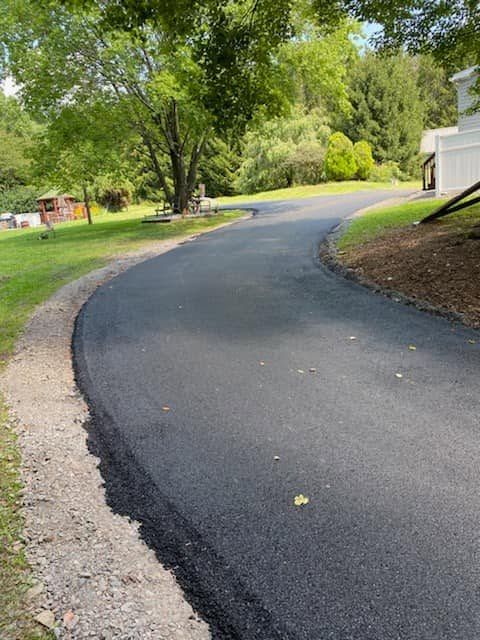 Curving paved driveway through a green yard beside a white house and trees