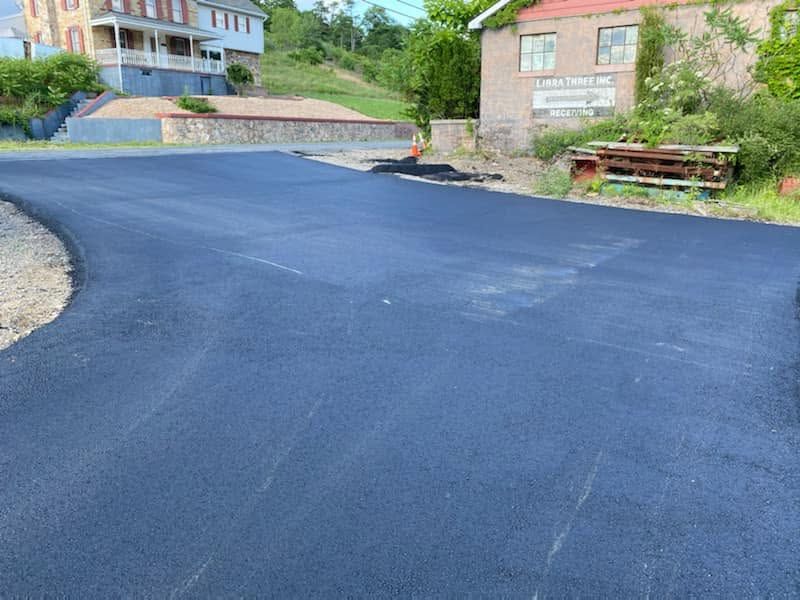 Freshly paved black asphalt driveway in front of houses and a stone wall