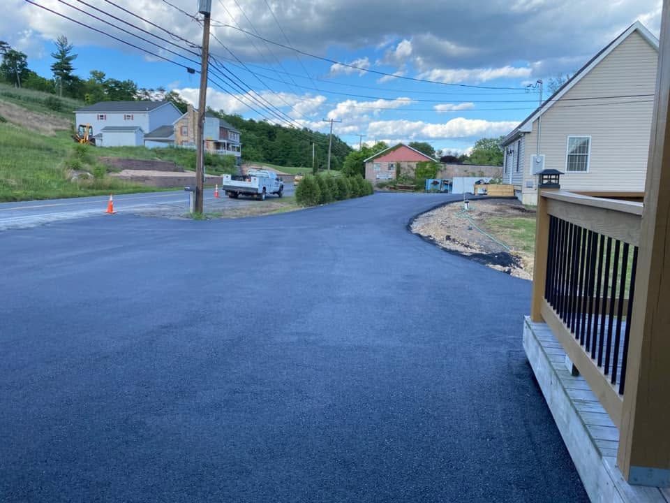 Freshly paved residential street with houses, utility poles, and a driveway beside a white building