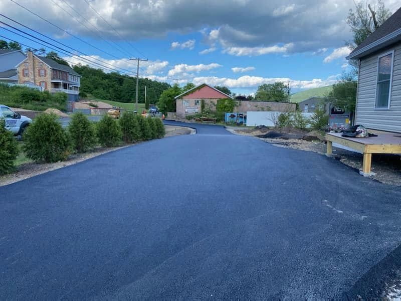Paved driveway beside homes and shrubs under a cloudy blue sky