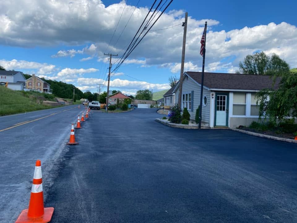 Freshly paved street with orange cones beside a small white building under a partly cloudy sky
