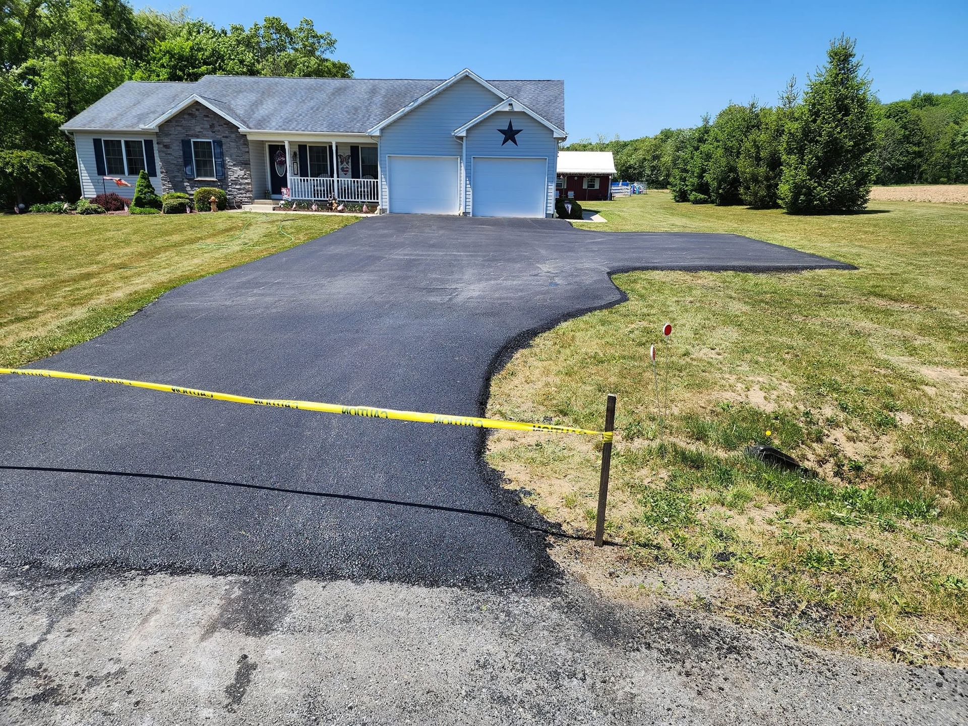 Suburban house with a freshly paved black driveway and yellow caution tape across the front edge
