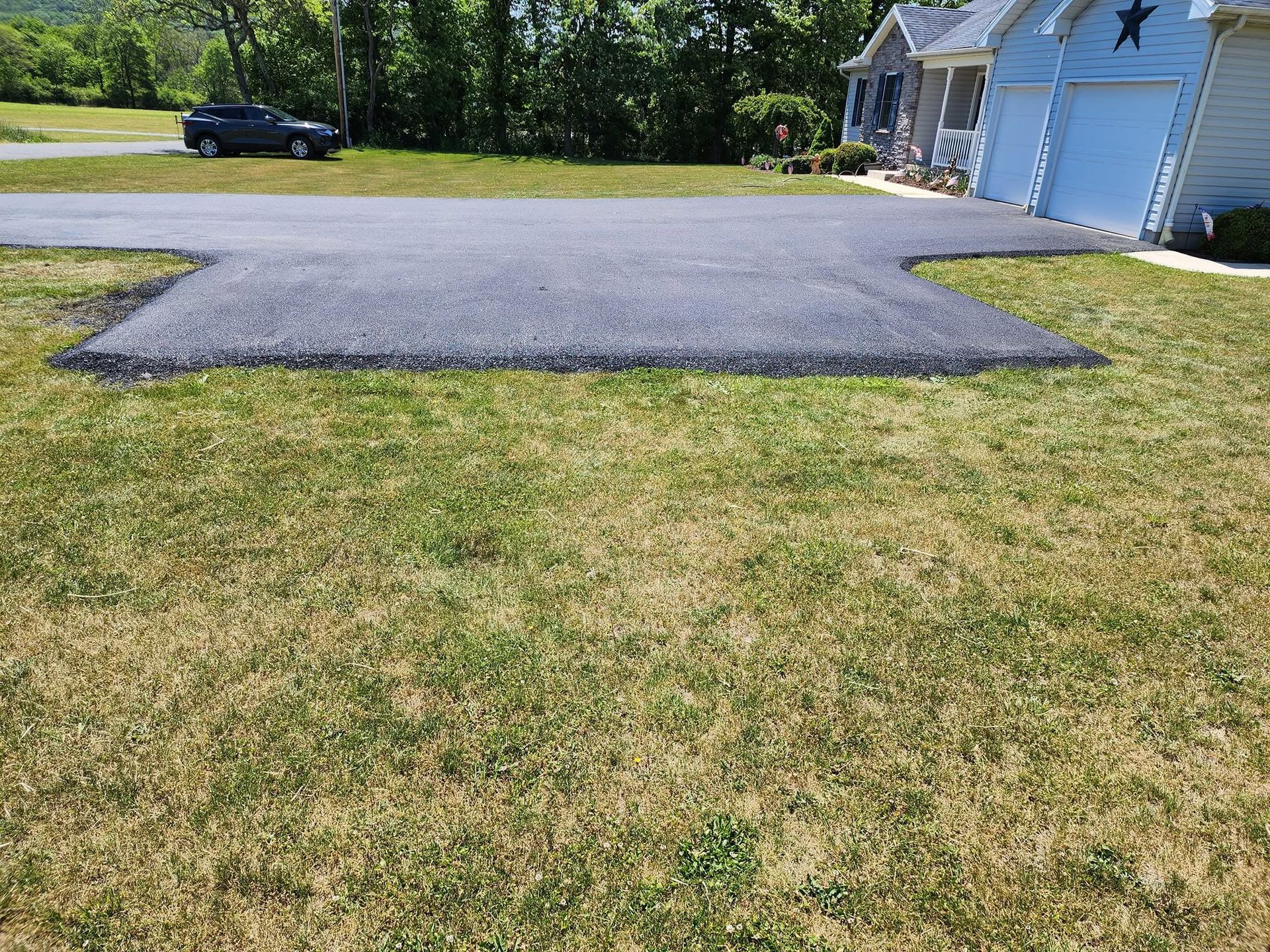 Gravel driveway apron in front of a house garage, bordered by grass, with a car parked near the road.