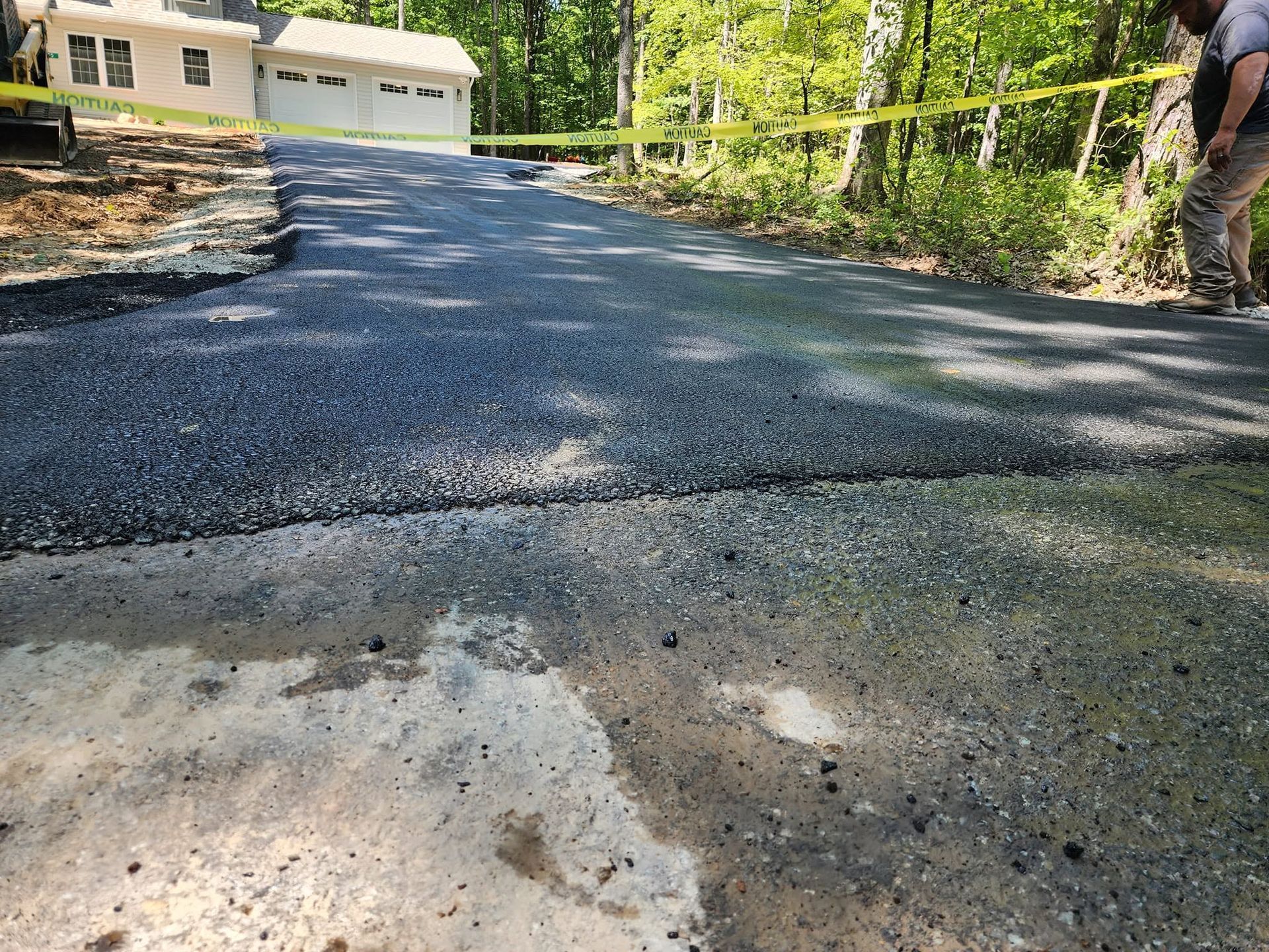 Freshly paved driveway leading to a house, with a worker standing at the right edge.