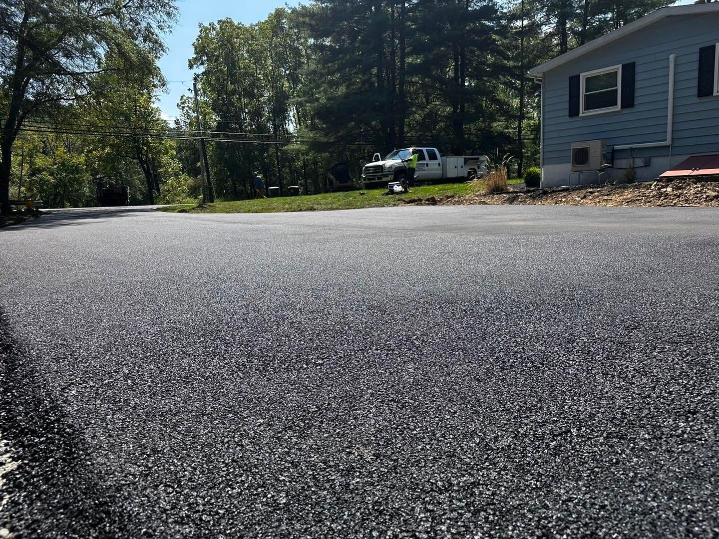 Fresh black asphalt road beside a house and trees on a sunny day