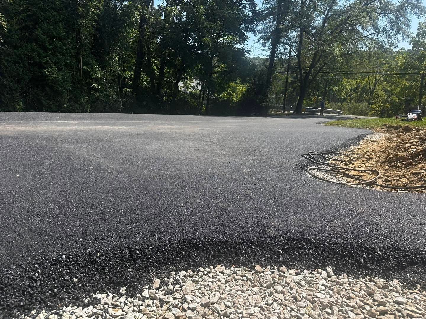 Cracked asphalt road with a pothole edge, bordered by trees and fallen leaves.