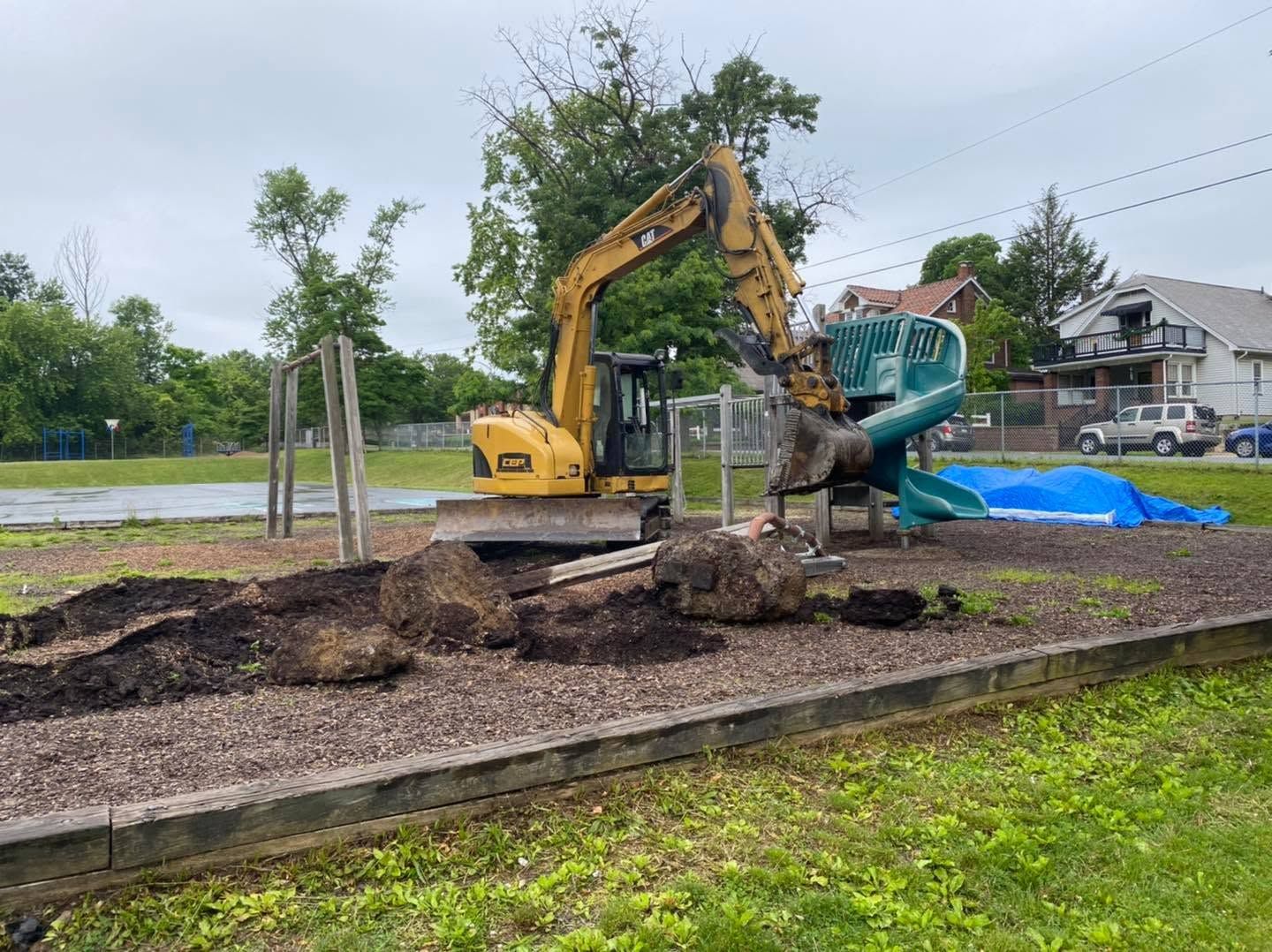 Excavator loading soil into a green dump truck at a roadside construction site