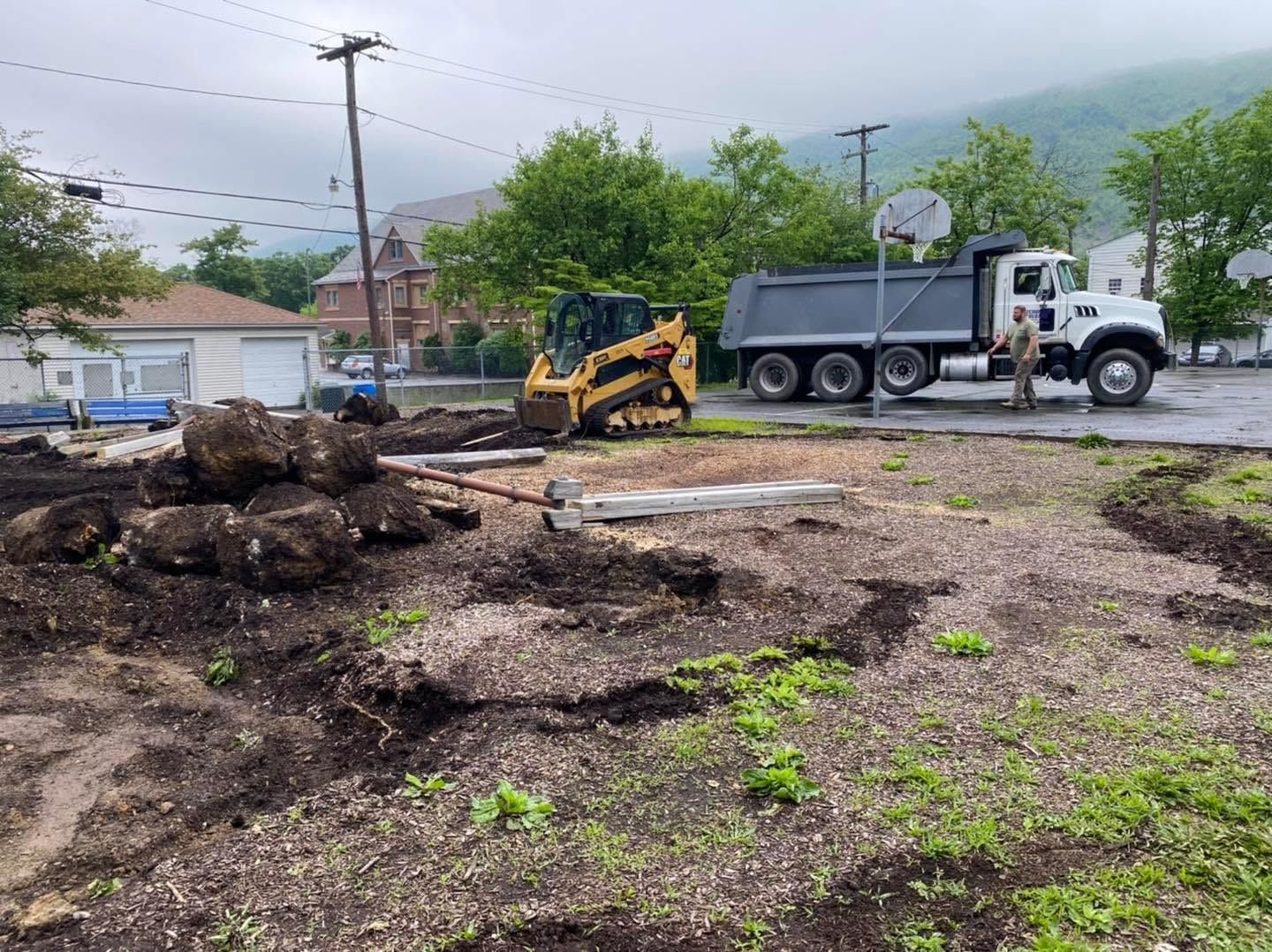 Construction site with a dump truck and backhoe beside a pile of soil and debris.