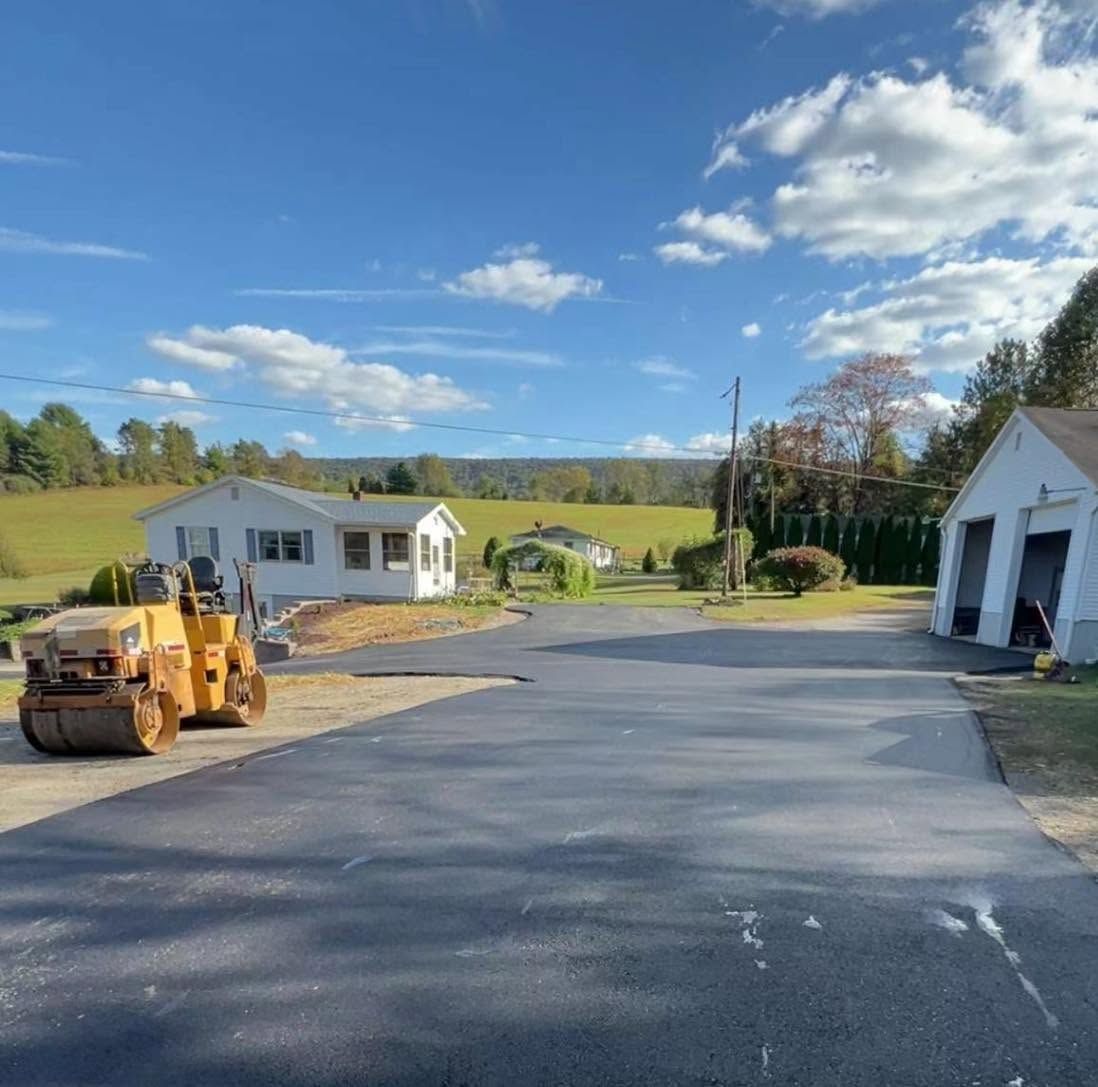 Freshly paved driveway with a yellow construction machine, house, and garage under a blue sky