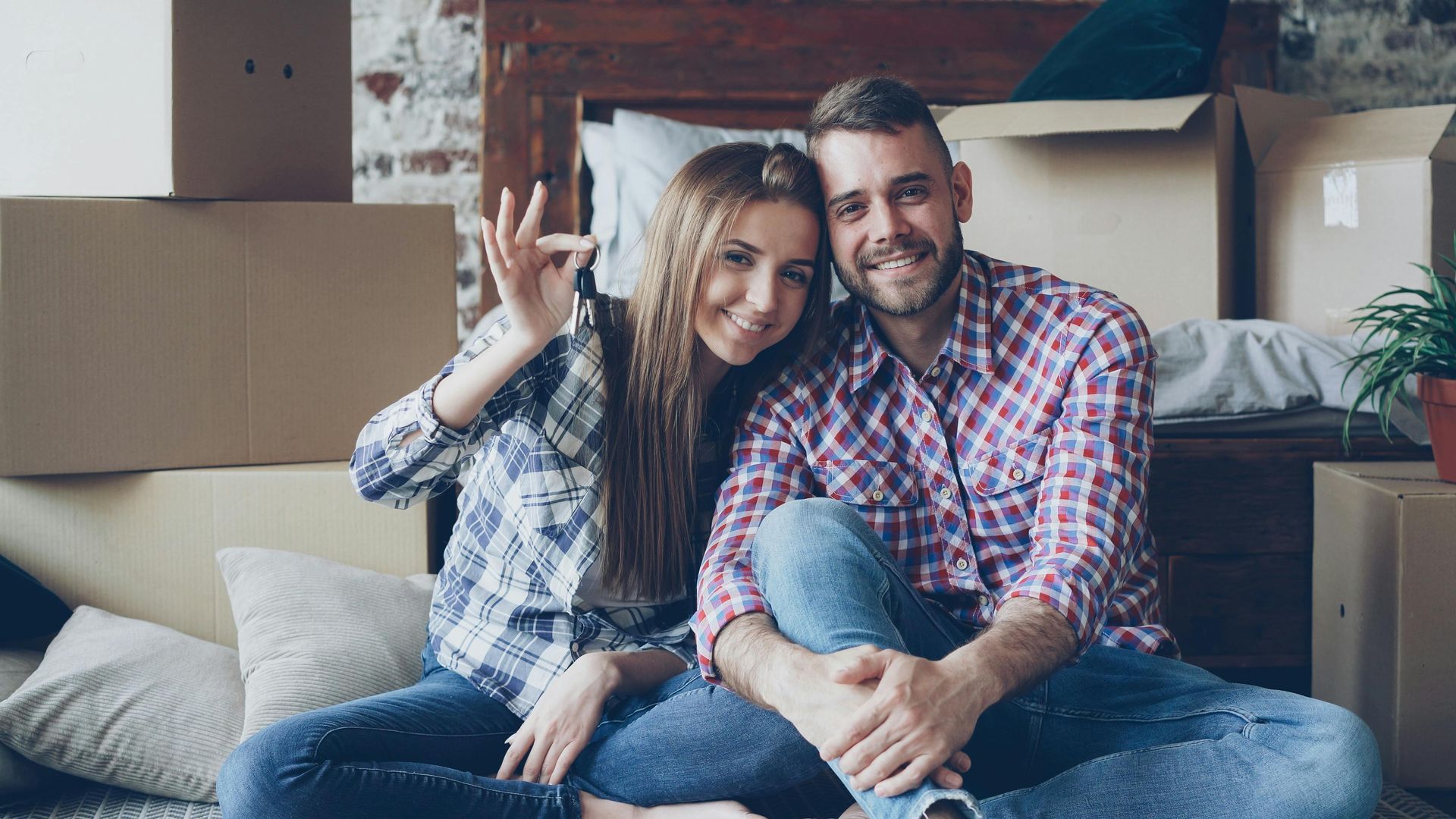 Smiling couple sitting on the floor among moving boxes, waving in a cozy living room