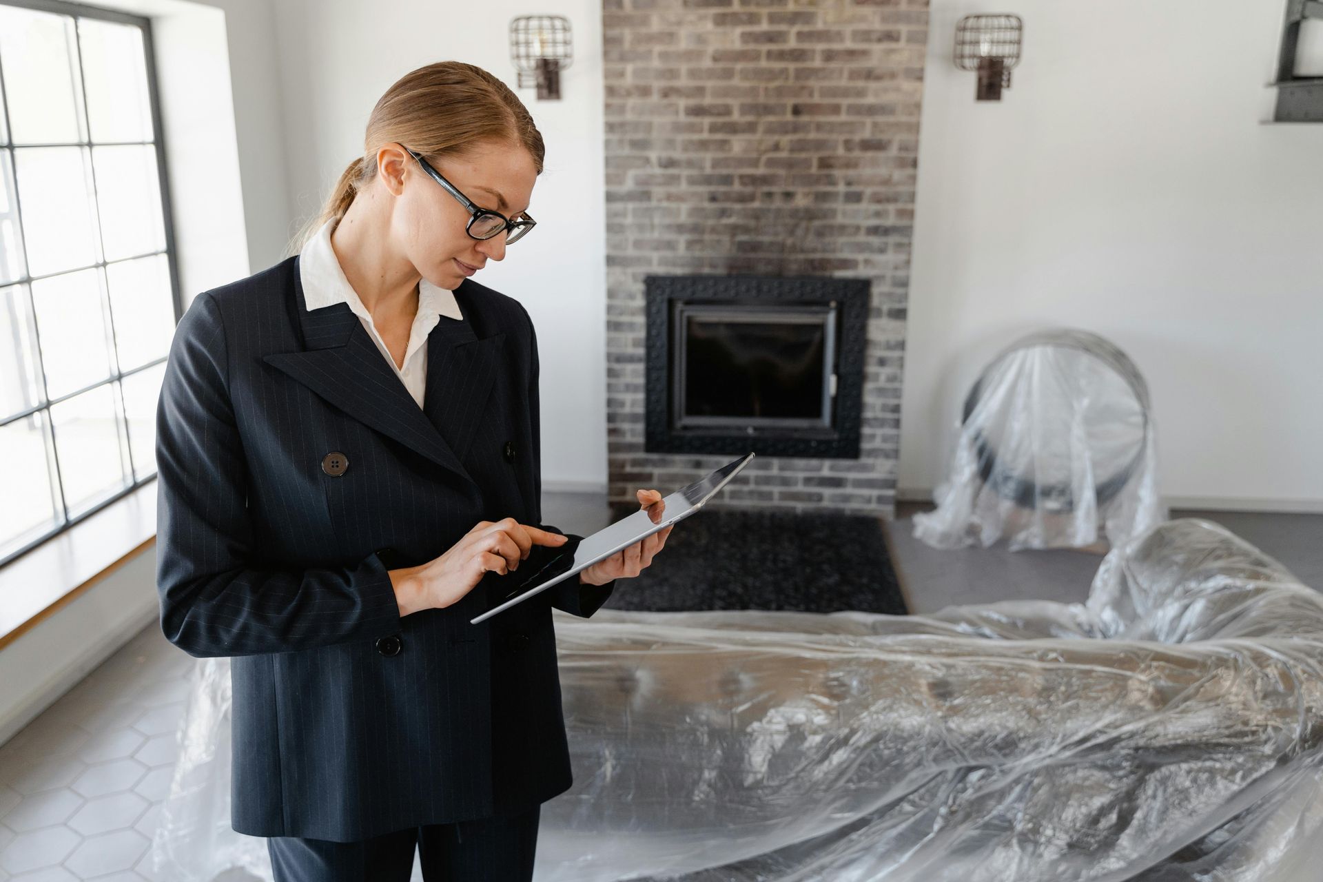 Person in a black suit using a tablet in a room under renovation, with furniture covered in plastic.