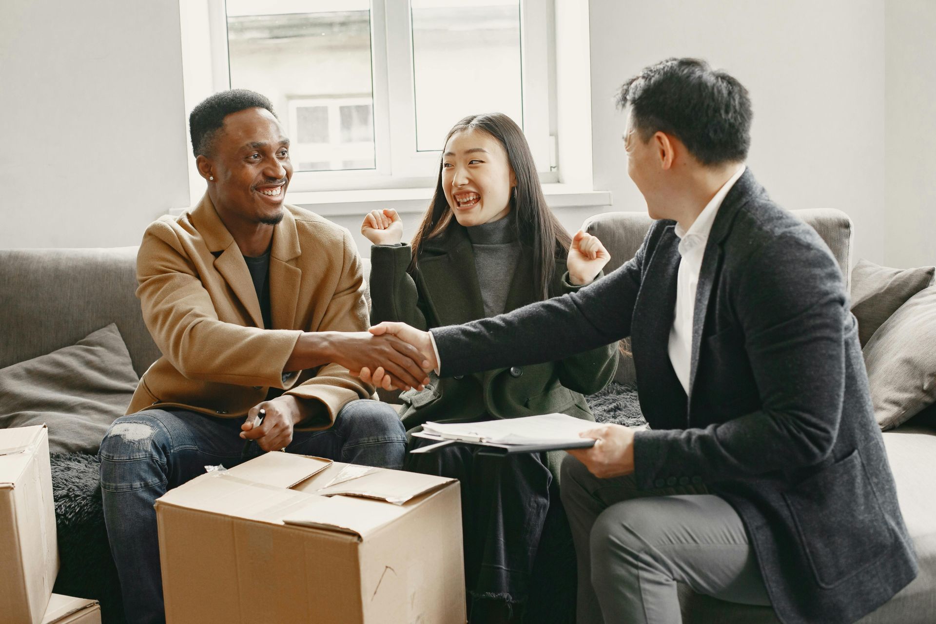 Three people shaking hands on a couch in a bright living room, smiling during a meeting