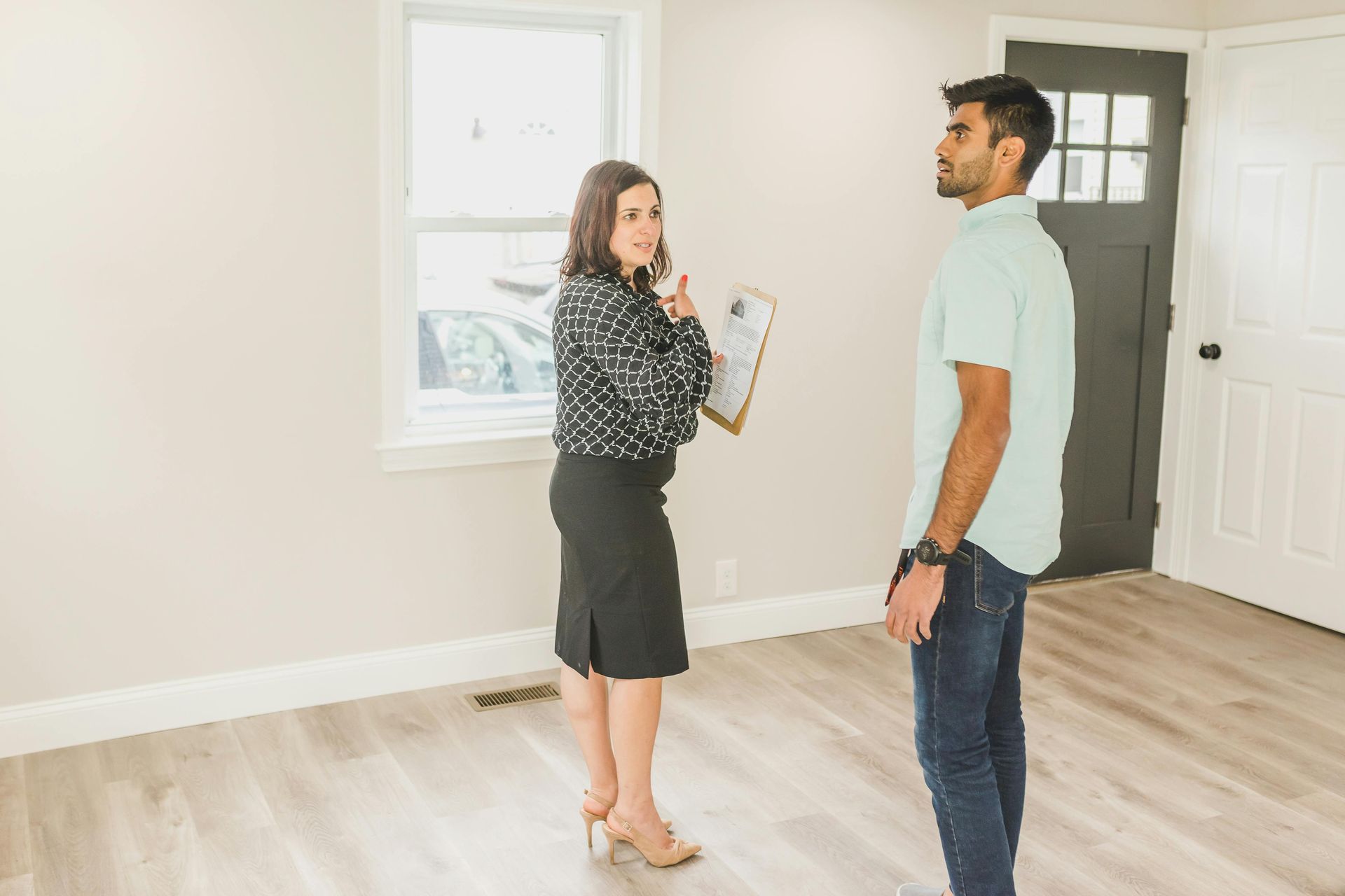 Two people talking in a bright empty room, one holding a clipboard during a home viewing.