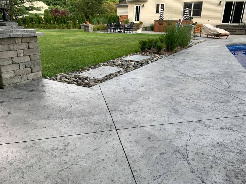 A concrete patio with a pool in the background and a house in the background.