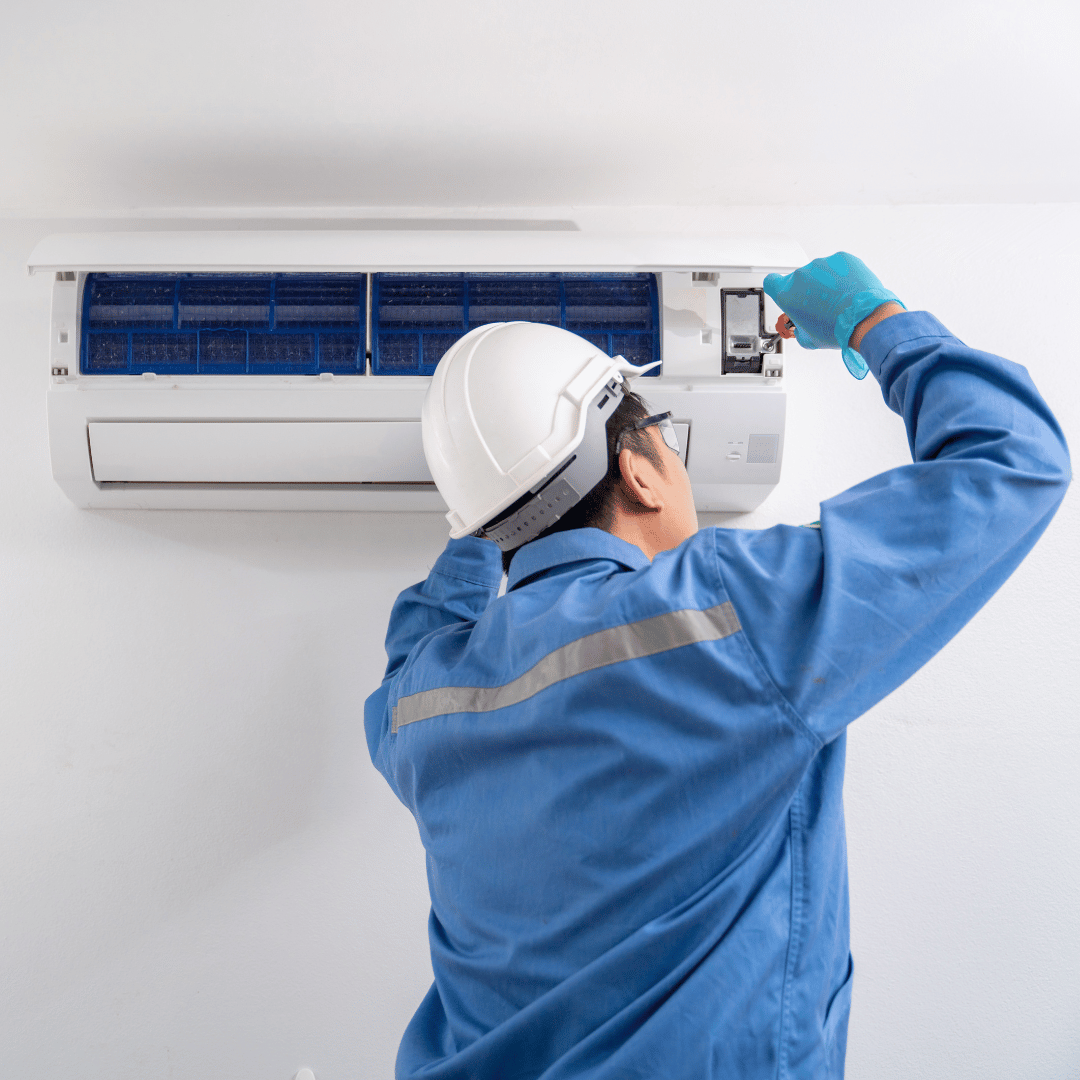 A man wearing a hard hat is working on an air conditioner.
