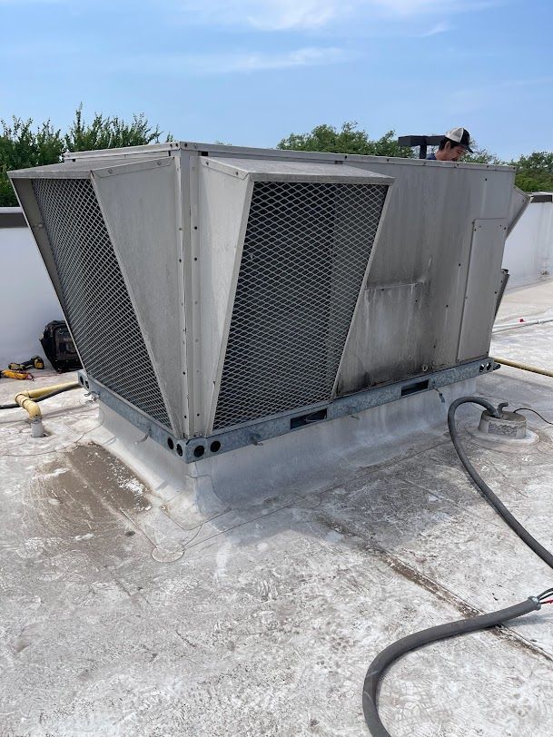 A man is working on a large air conditioner on top of a roof.