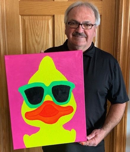 A man is holding a painting of a duck wearing sunglasses