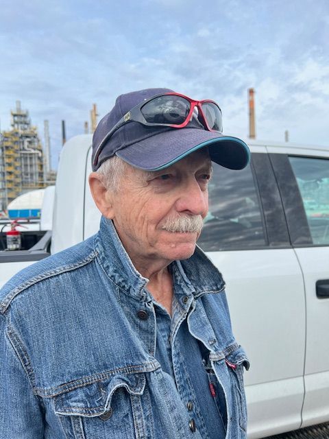 A man wearing a hat and sunglasses is standing in front of a white truck.