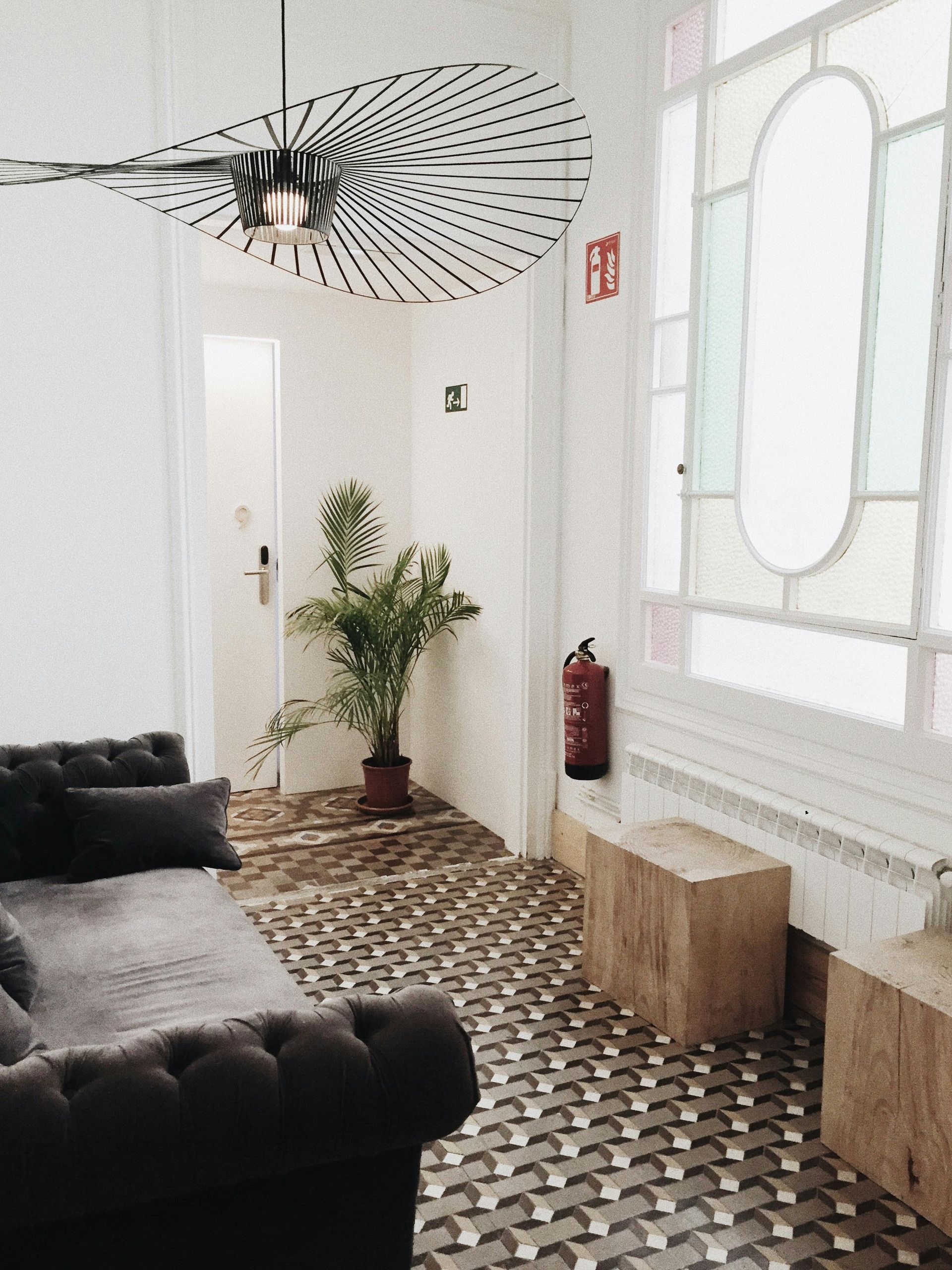 Stylish entry hall with patterned tile floor, tufted sofa, wooden benches, and large stained-glass window.