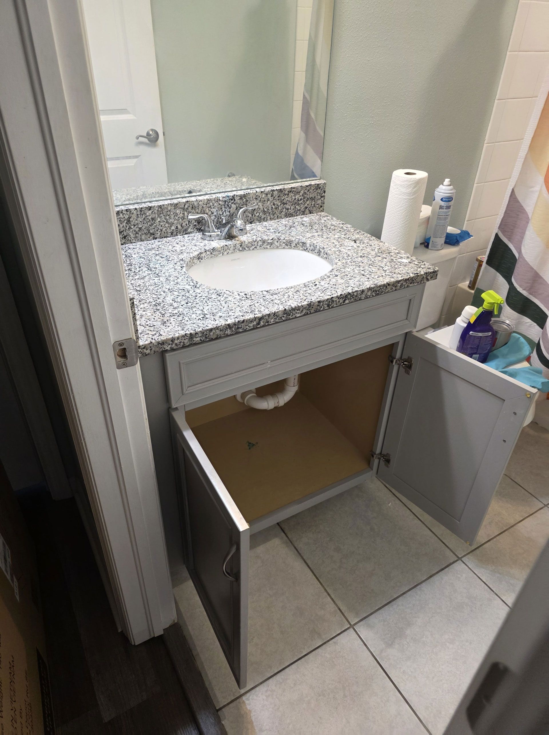 Bathroom vanity with gray cabinets, granite countertop, open doors.