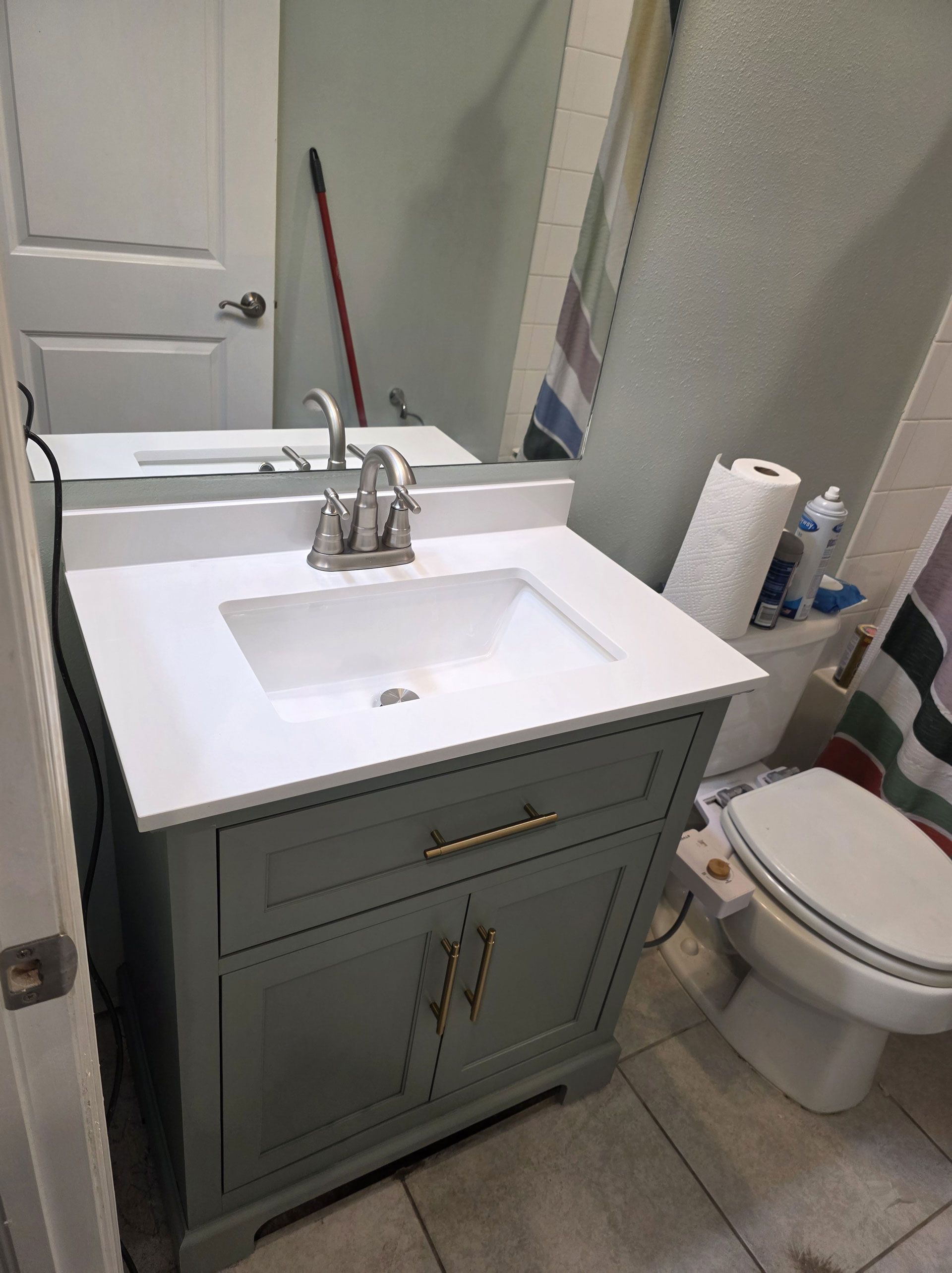 Bathroom vanity with a white countertop and a gray cabinet. Includes a sink, mirror, and toilet.