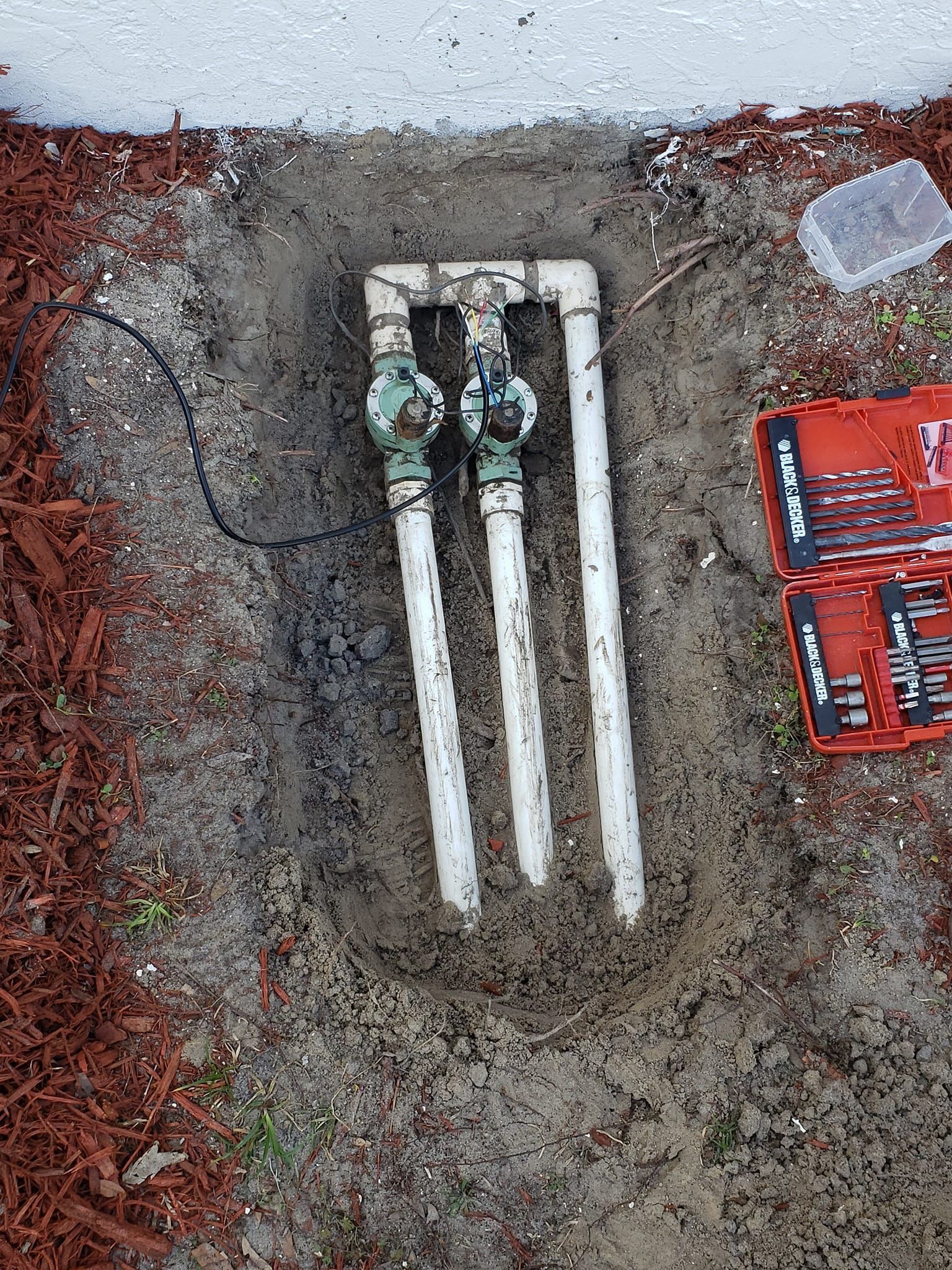 Sprinkler system components in a hole in the ground, with a toolbox beside it.