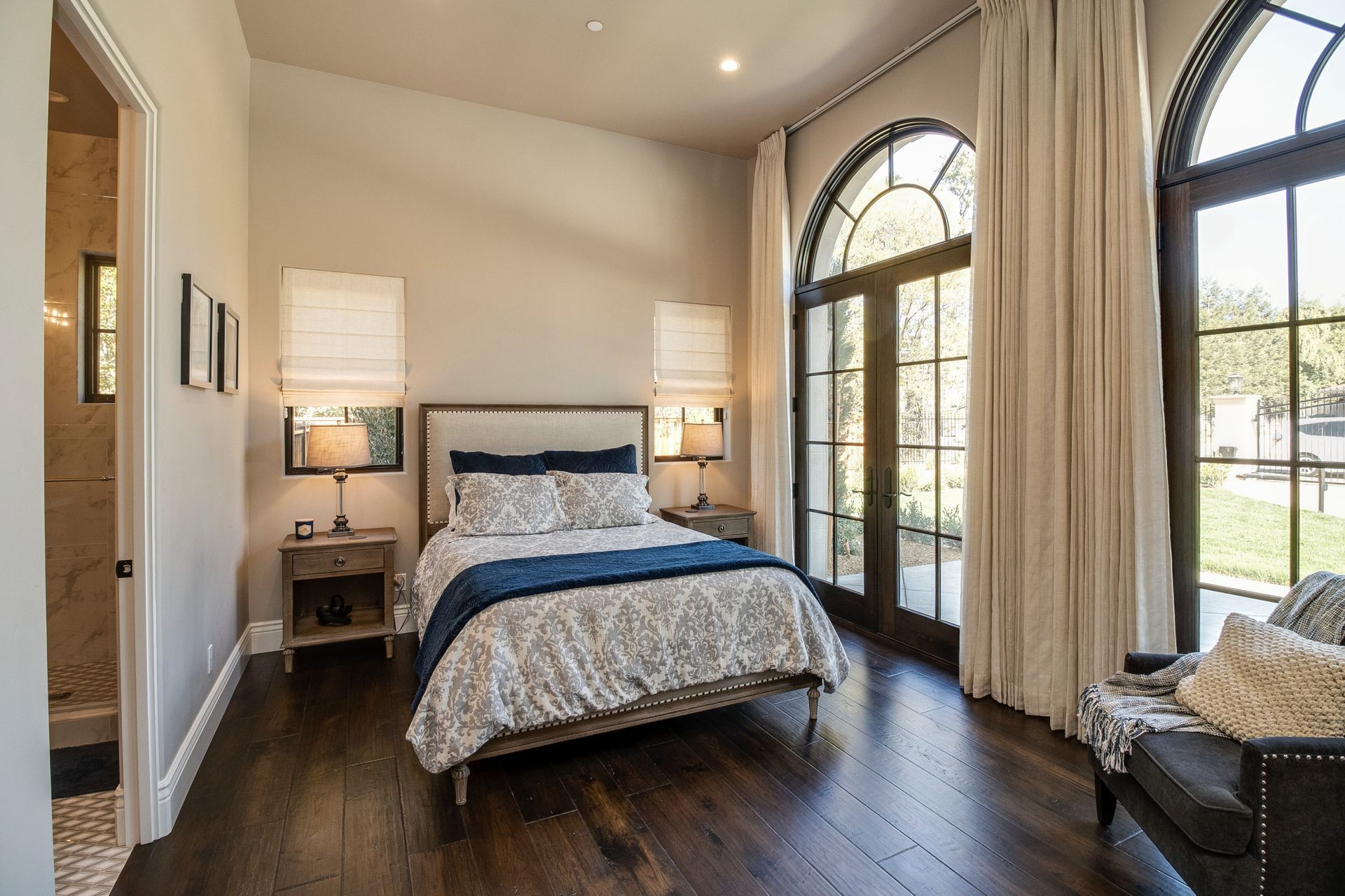 A bedroom with a bed , chair , nightstand , and large windows.