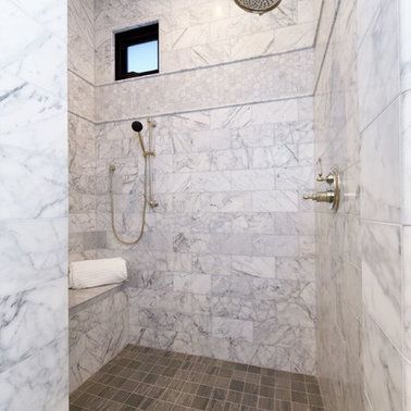 A walk in shower with marble tiles and a window.