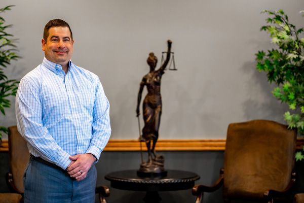 Brendan Burke posing in front of a small bronze statue of Lady Justice