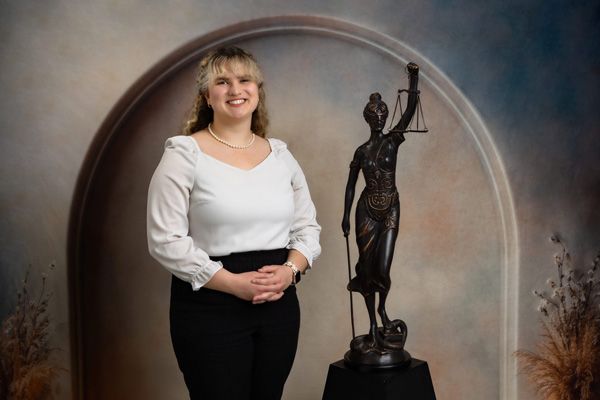 Caden Butler posing in front of a small bronze statue of Lady Justice