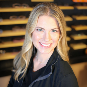 A woman is smiling in front of a display of glasses