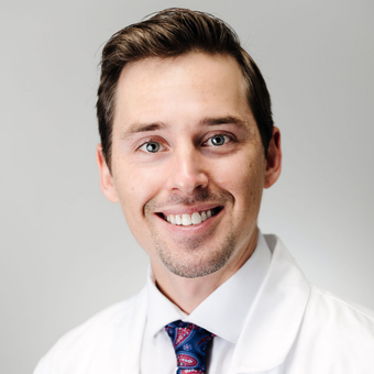 A man in a white coat and tie smiles for the camera