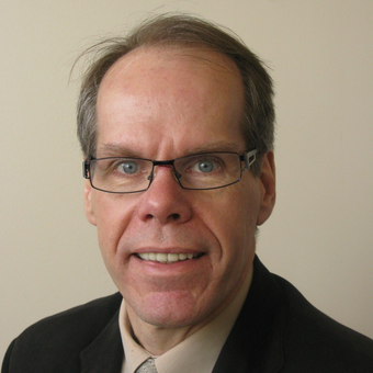 A man wearing glasses and a suit smiles for the camera