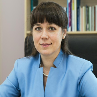A woman in a blue jacket sits in front of a bookshelf