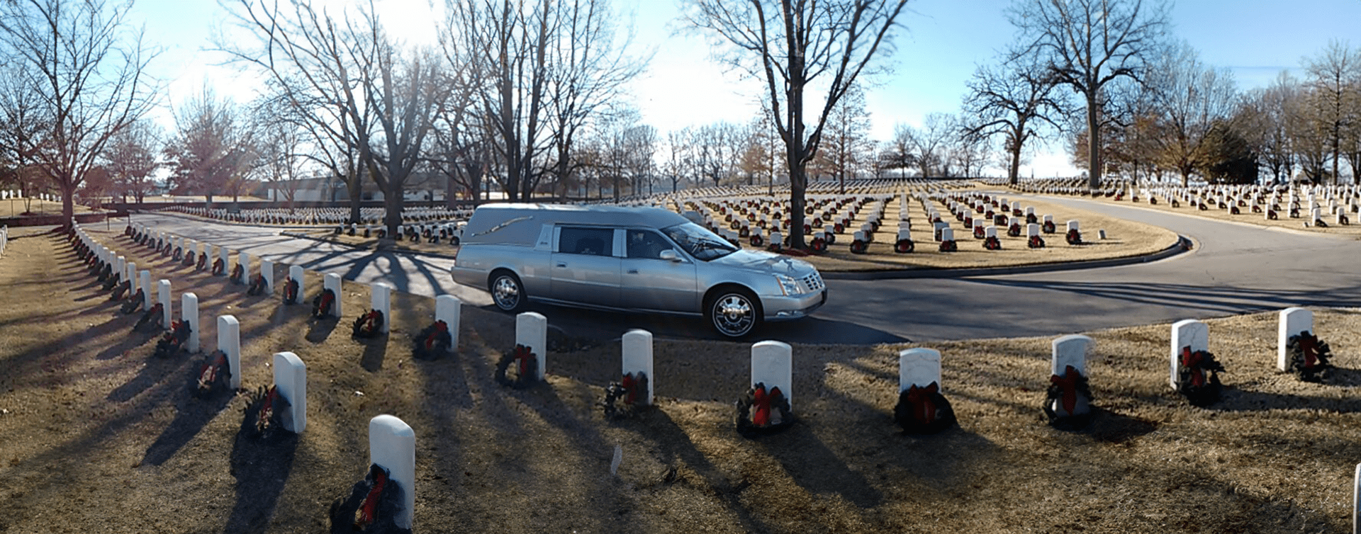 Silver minivan parked near a circular memorial with white stone markers and bare trees in winter