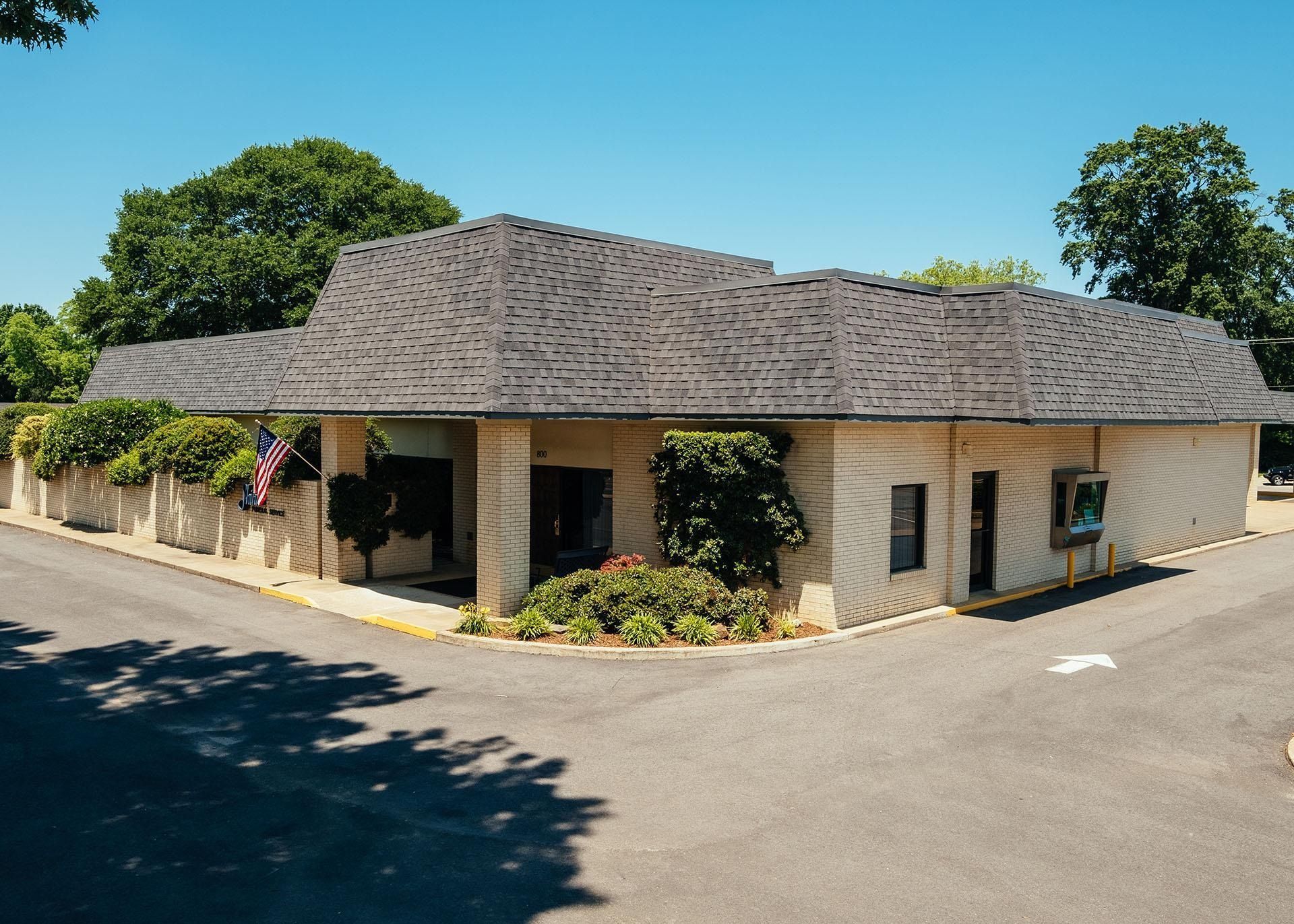 Single-story beige office building with a dark shingled roof, surrounded by trees and a parking lot.