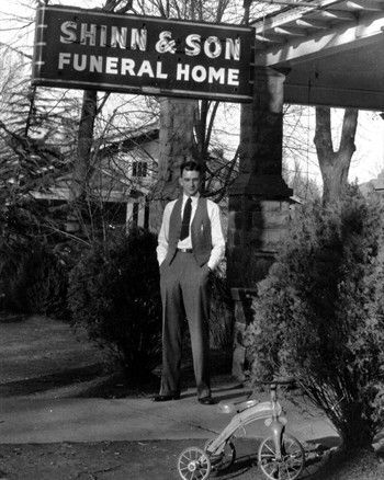 Man standing outside Shinn & Son Funeral Home beside a tricycle