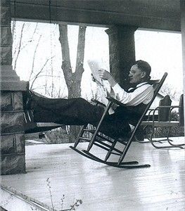 Man reclining in a rocking chair reading a book on a screened porch