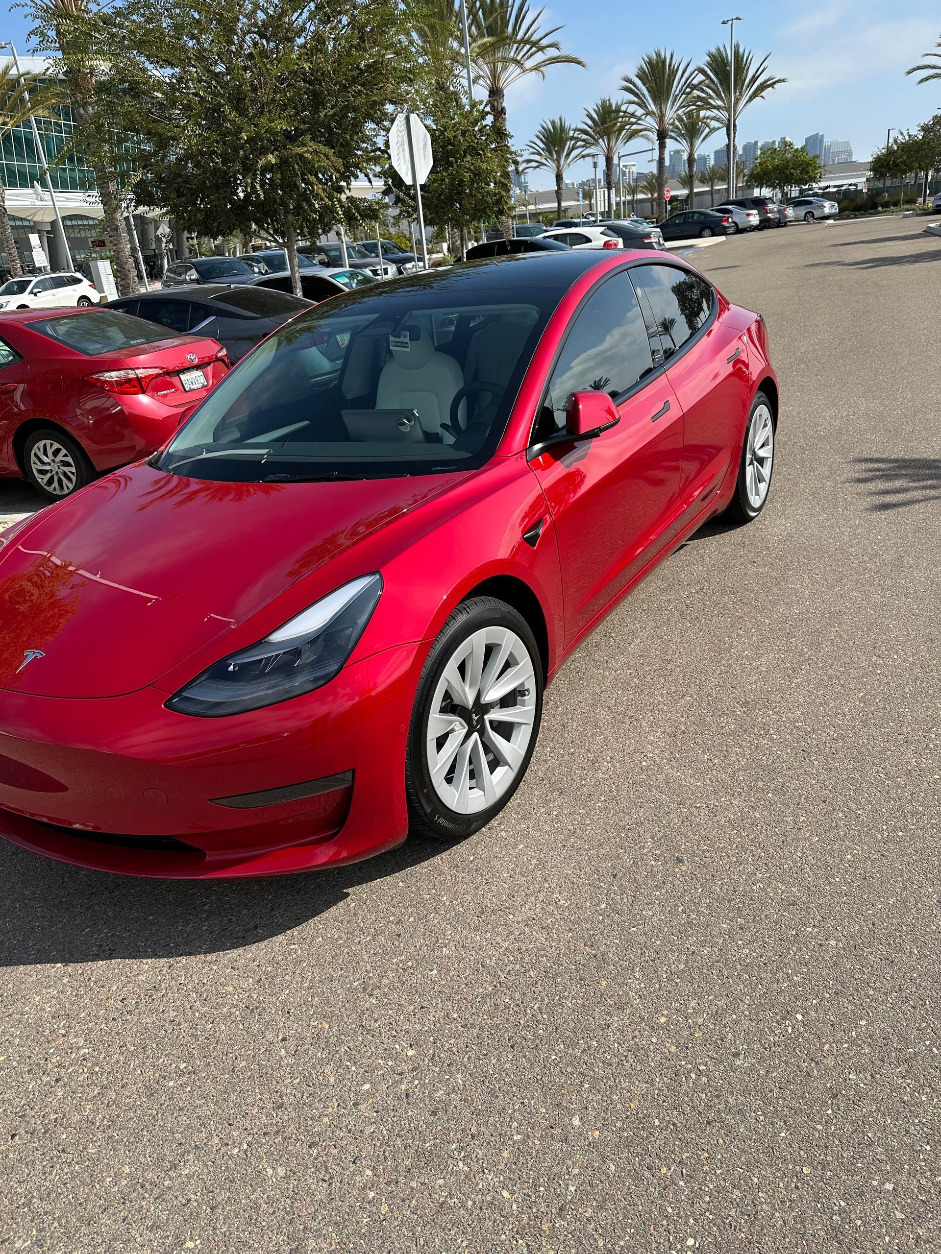 A red tesla model 3 is parked in a parking lot.