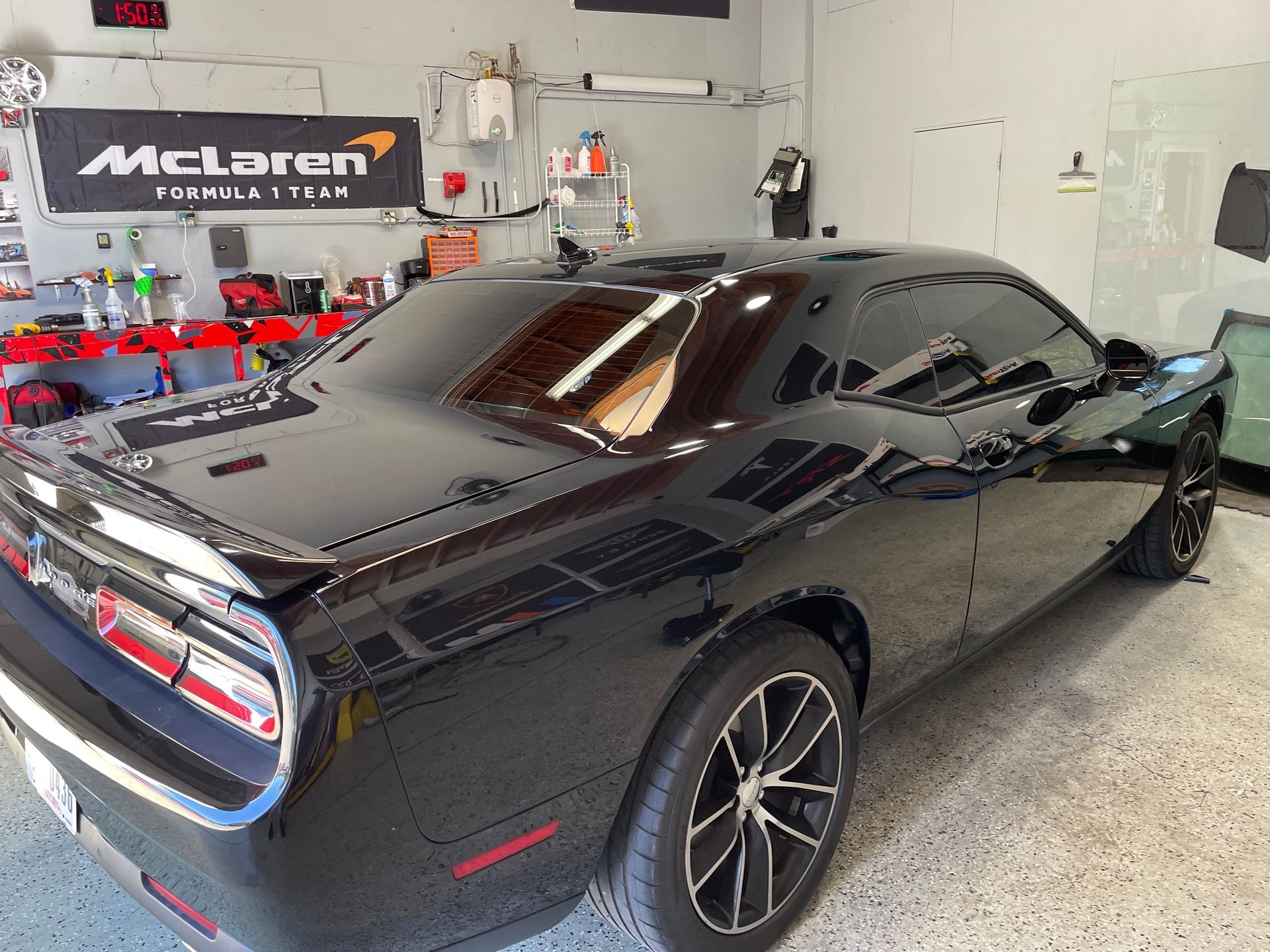 A black dodge challenger is parked in a garage next to a mclaren sign.