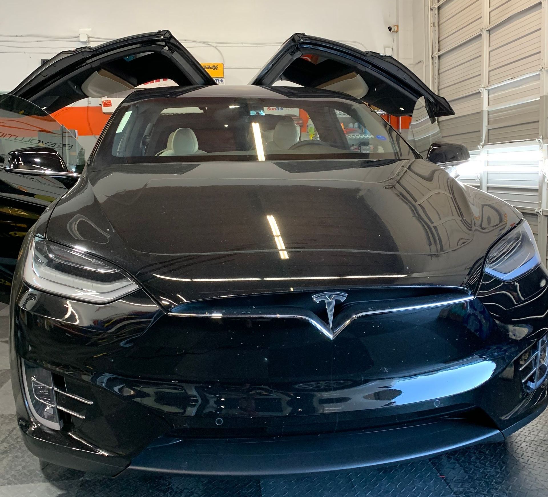 A black tesla model x is parked in a garage with its doors open.