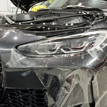 A close up of a car with its hood open and headlights wrapped in plastic.