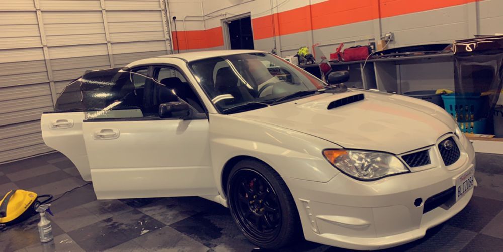 A white subaru is parked in a garage with its doors open.