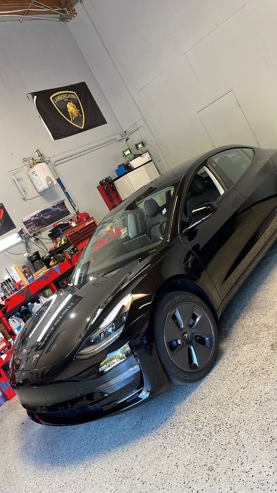 A black tesla model 3 is parked in a garage.
